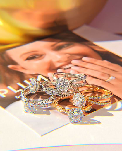 Several shimmering diamond rings are arranged on a photo featuring a smiling woman’s face, with one ring on her finger.