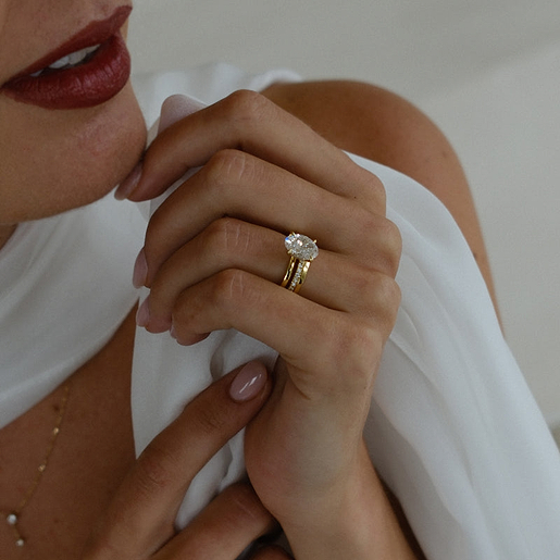 Yellow gold oval engagement ring and wedding band on hand.