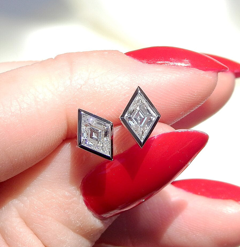 woman's hand holding a pair of lozenge shaped stud earrings
