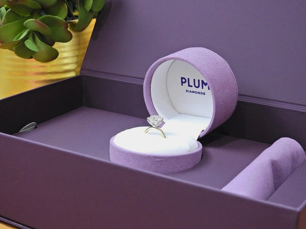 a Plum Diamonds engagement ring in a circular violet ring box inside a larger plum box