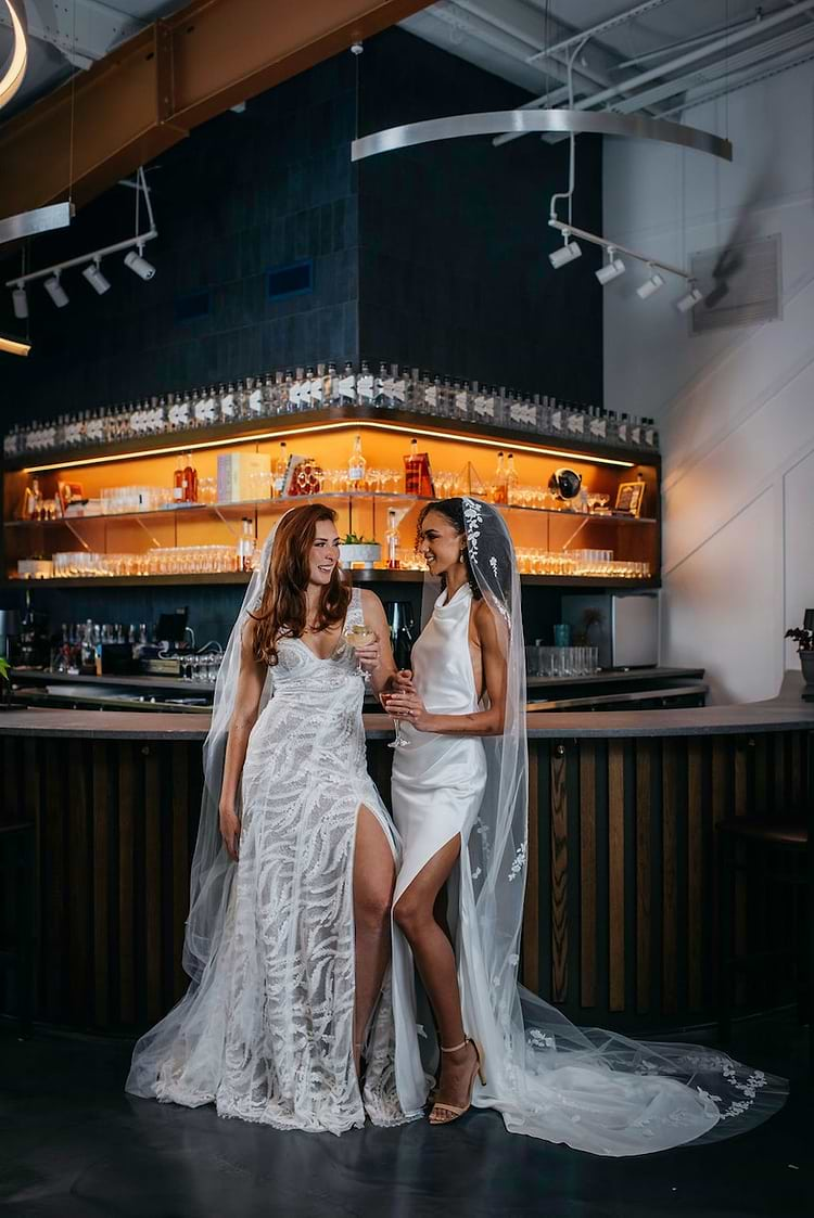 two women in bridal gowns standing at a bar