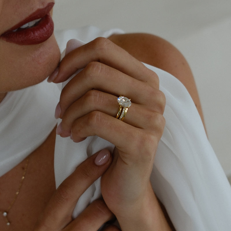 Oval cut engagement ring and wedding band on hand.