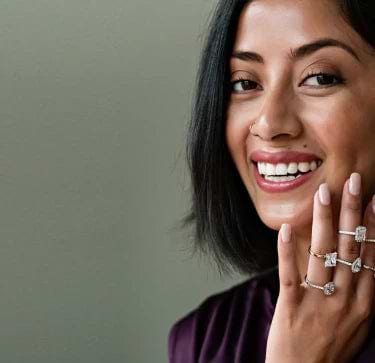  woman with a hand up to face displaying multiple diamond rings smiling