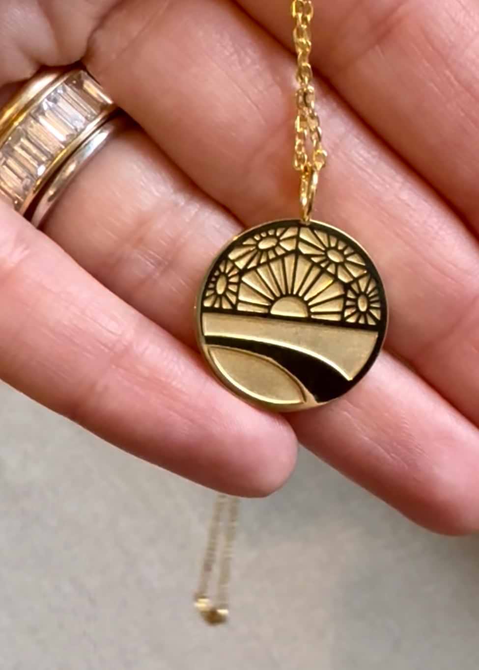 Gold necklace with a circular pendant held by a hand on a neutral background