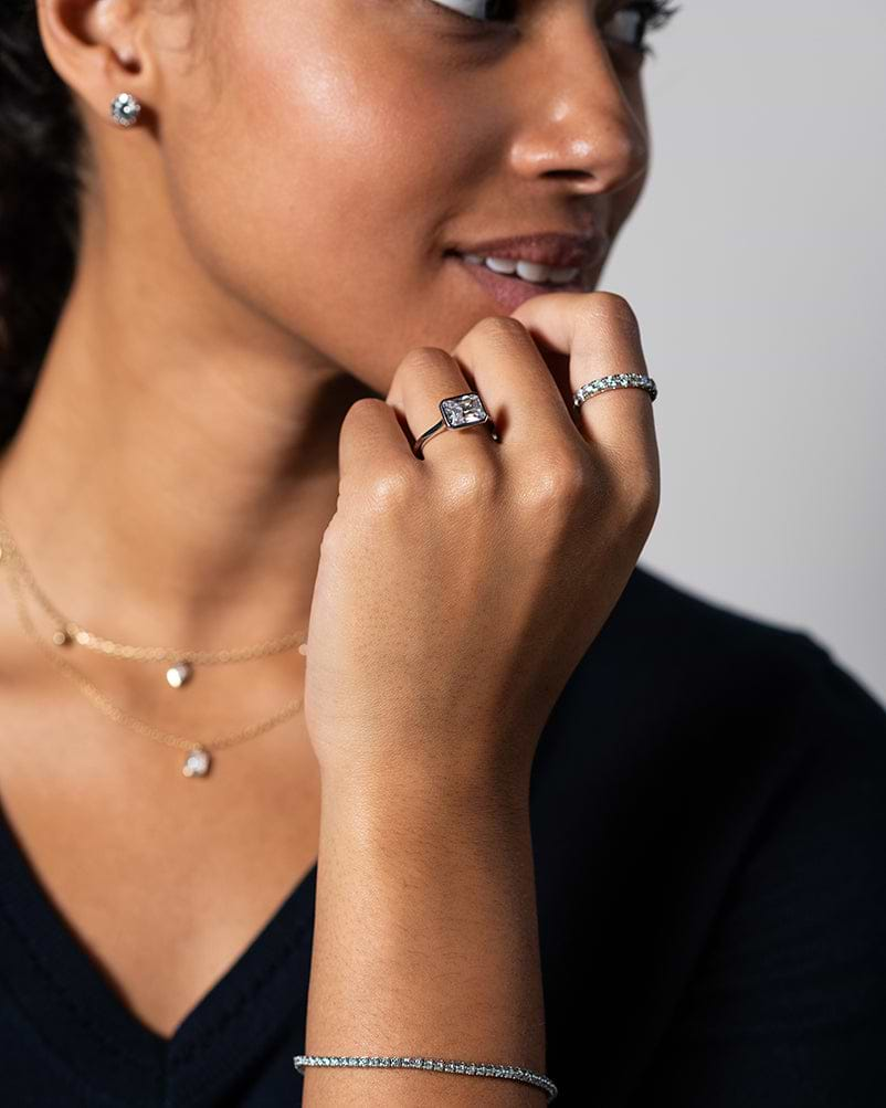 smiling woman holding her hand up wearing white gold diamond rings and bracelet