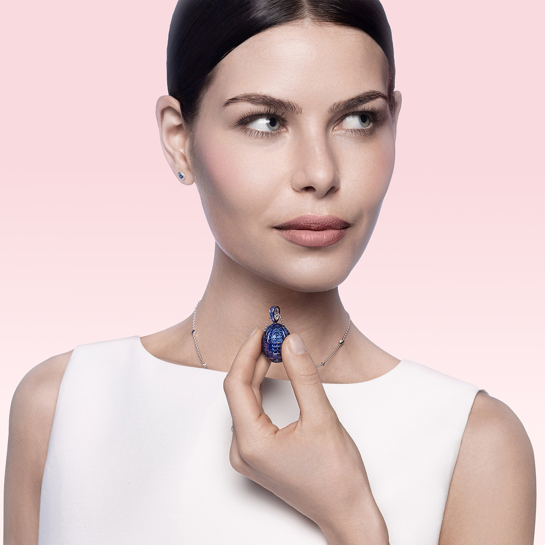 Woman holding a blue gemstone Fabergé necklace against a pink background