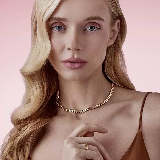 Woman wearing a Fabergé gold necklace and ring against a pink background