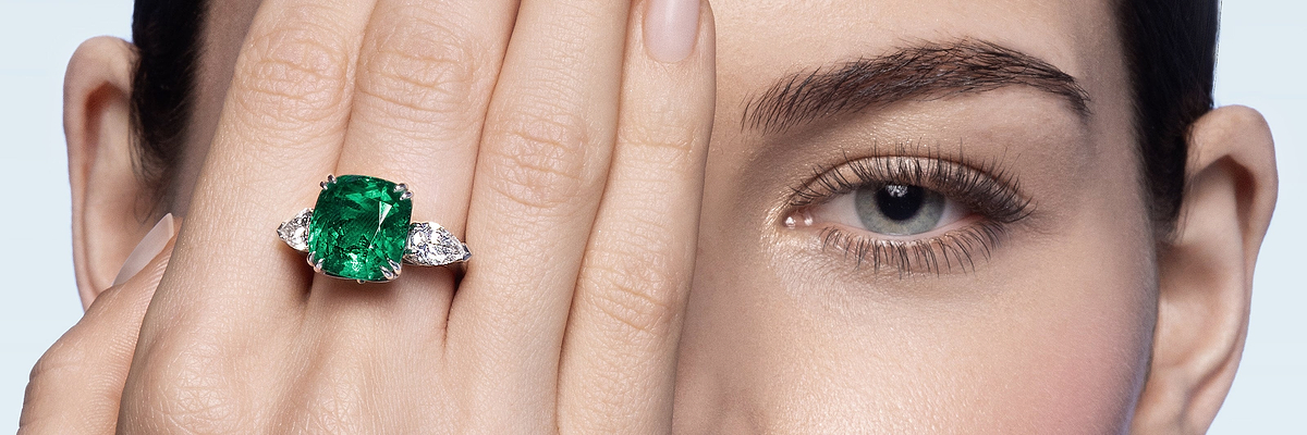 Close-up of a hand with a Fabergé emerald gemstone ring against a neutral background