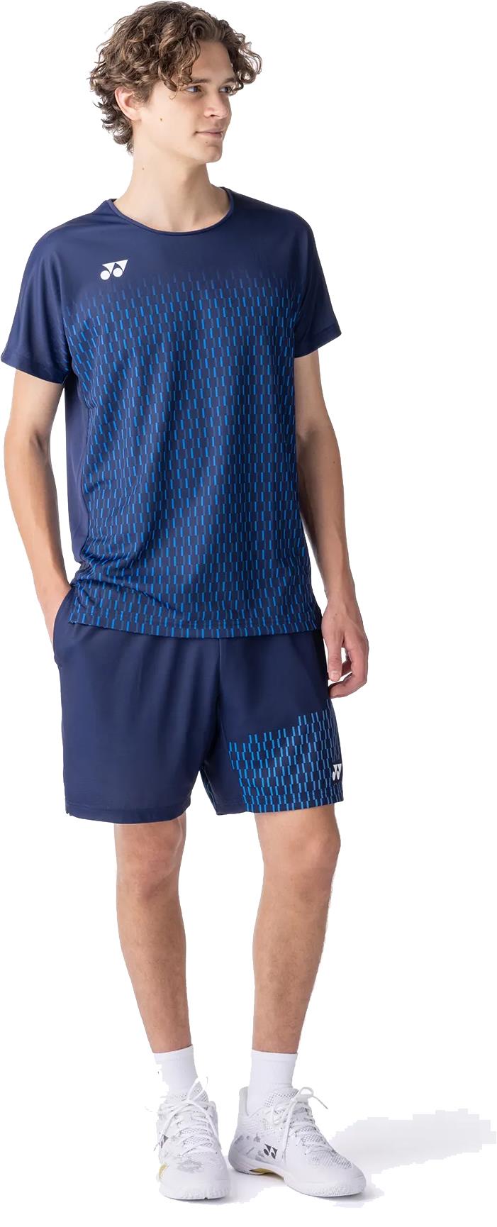 A young man stands with his hands in his pockets, wearing the Yonex 10713EX Crew Neck Men's Badminton T-Shirt in dark navy, paired with matching shorts and white shoes, highlighting its advanced moisture management against a white background.