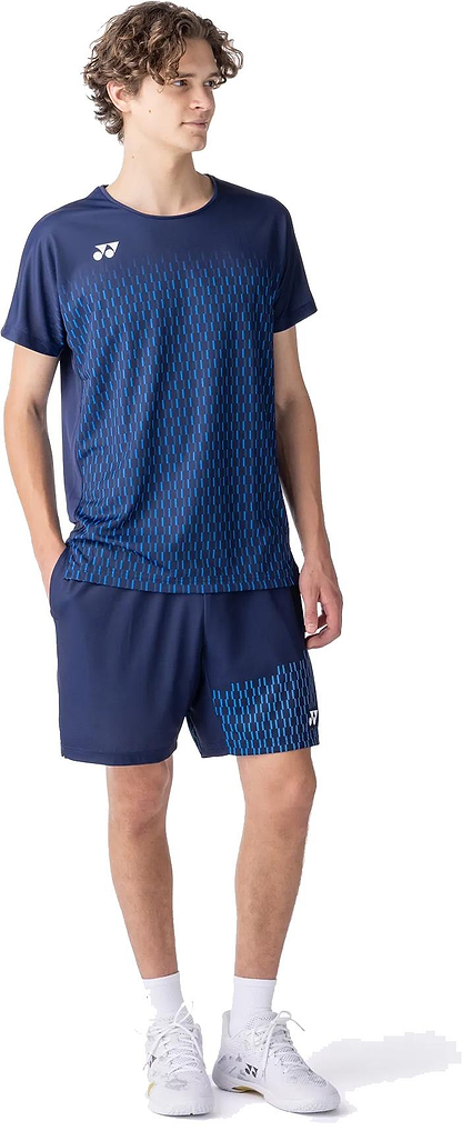 A young man stands with his hands in his pockets, wearing the Yonex 10713EX Crew Neck Men's Badminton T-Shirt in dark navy, paired with matching shorts and white shoes, highlighting its advanced moisture management against a white background.