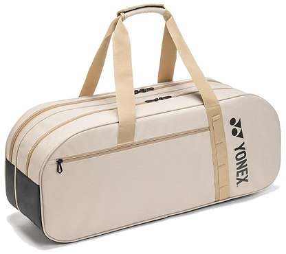 The Yonex BA72631WEX Gearlogic Tournament Badminton Bag in beige features tan handles, black ends, a side pocket with a black Yonex logo, and multiple zippered compartments—ideal for tournaments.