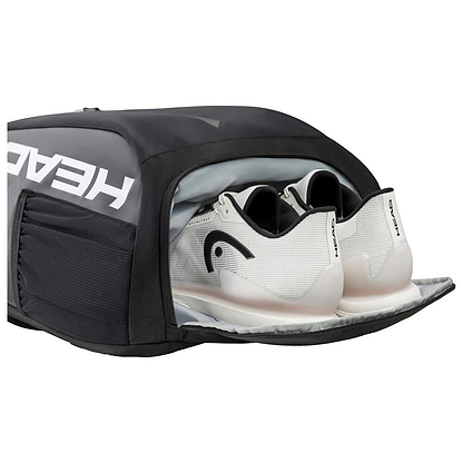 A black sports bag with a shoe compartment is open, showing white athletic shoes inside. The bag, marked with "HEAD" in bold white letters, resembles the HEAD Tour Badminton Backpack - Black / White, known for its generous space for gear and a dedicated racket compartment.