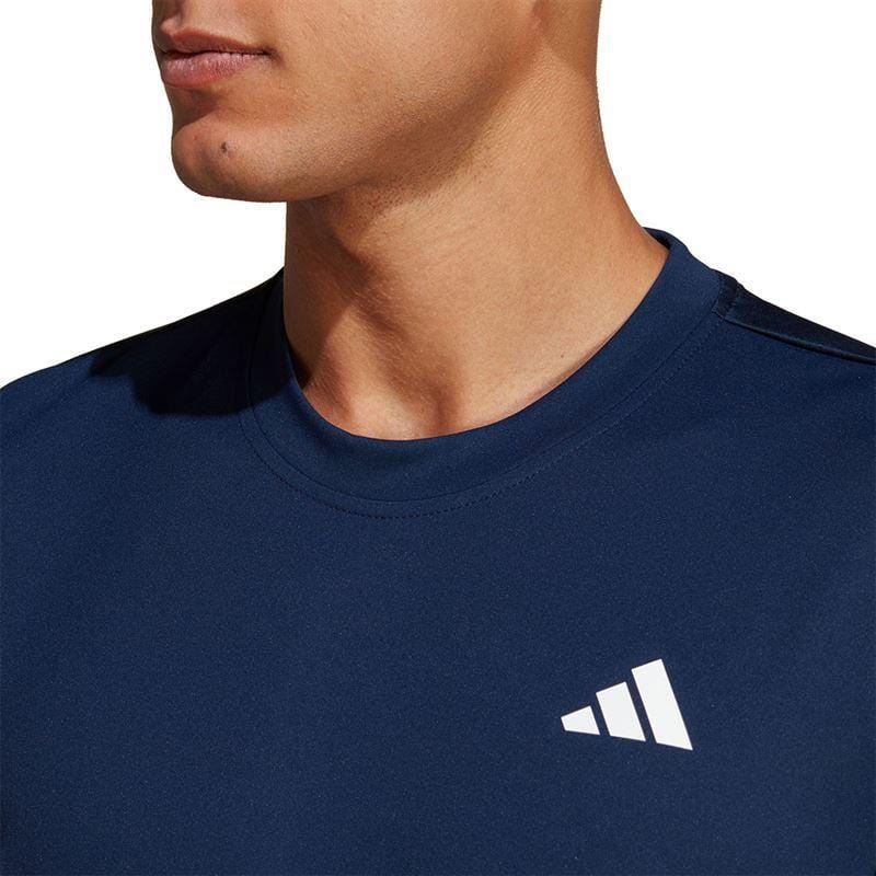 A person is wearing a navy ADIDAS Mens Club Badminton T-Shirt from adidas, featuring a white stylized triangular logo on the chest. The focus is on the upper torso and neck, with the face partially visible. The shirt is crafted from sporty, lightweight AEROREADY fabric.