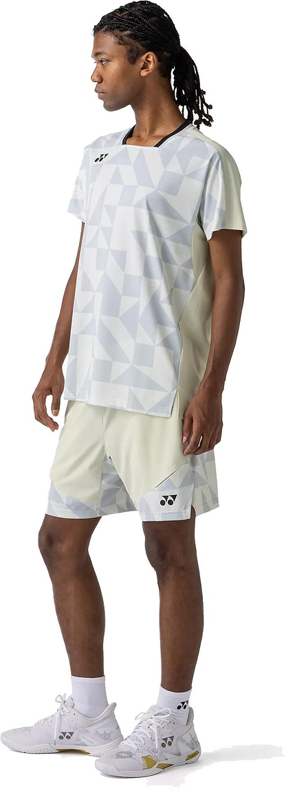 A person in a light-toned Yonex 10712YX Crew Neck Men's Badminton T-Shirt - Champagne, faces slightly left. The sporty look features the Yonex shirt, shorts, white socks, and white athletic shoes.