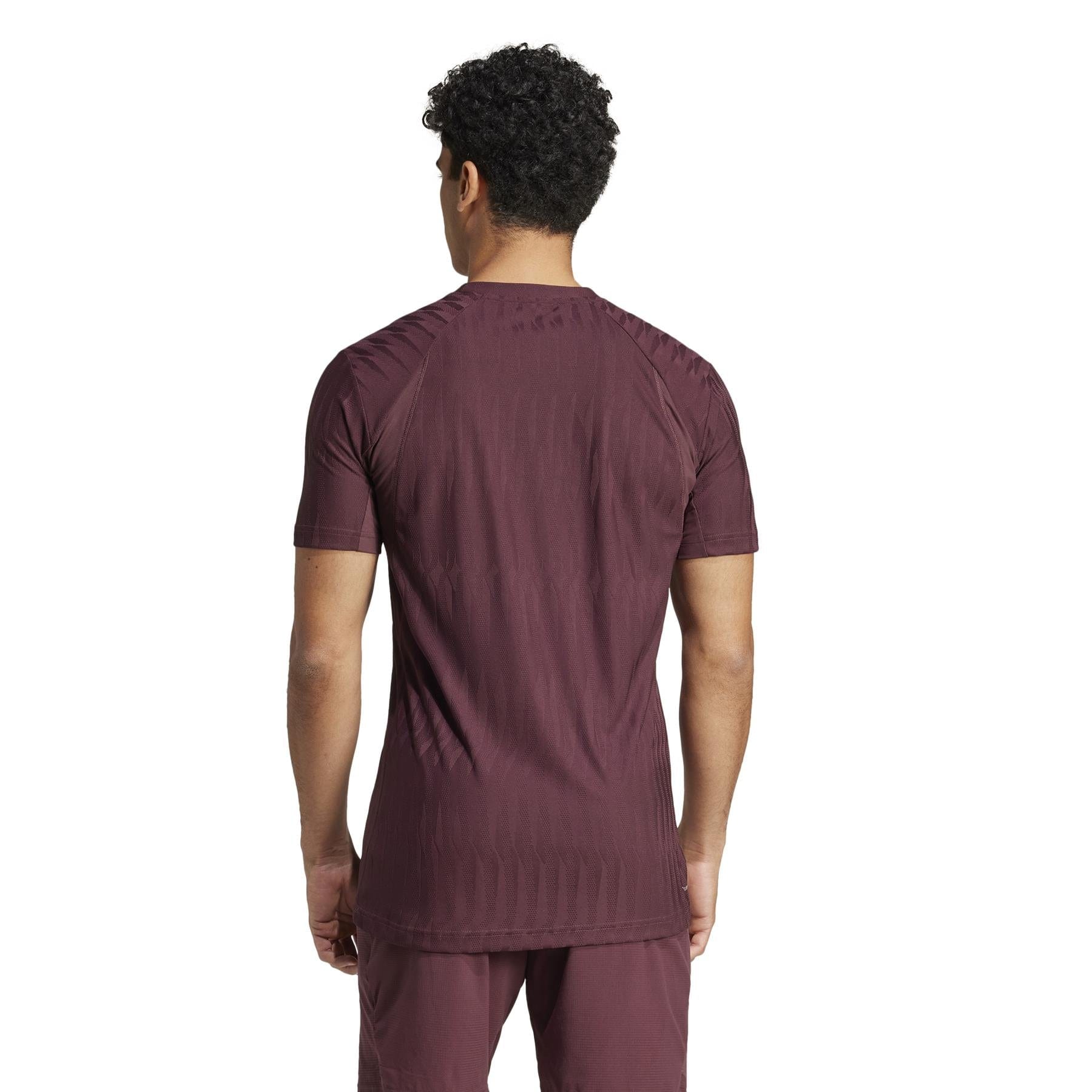 A person with curly black hair wears the ADIDAS Men's Climacool+ Freelift Badminton T-Shirt in Ruby by adidas, made from recycled materials, viewed from the back against a plain white background.