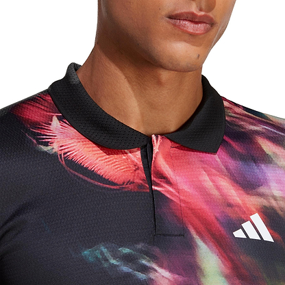 A close-up of a person wearing the adidas Melbourne Men's Freelift Polo Shirt, featuring vibrant abstract patterns and HEAT.RDY technology. The shirt, designed in black and multi-colored hues, includes a striking white Adidas logo on the chest for added style and performance.