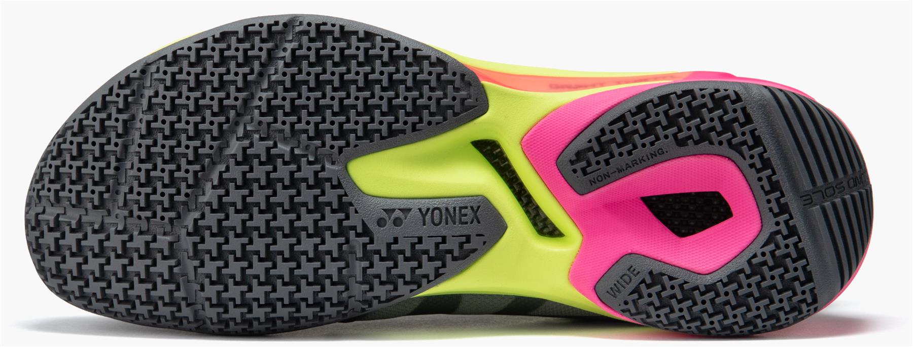 Close-up of the Yonex Subaxia GT WIDE Unisex Badminton Shoes in grey, showing a textured black and gray sole with neon yellow and bright pink accents. The Yonex logo appears near the center, emphasizing GRPHT THRTTL technology for better performance.