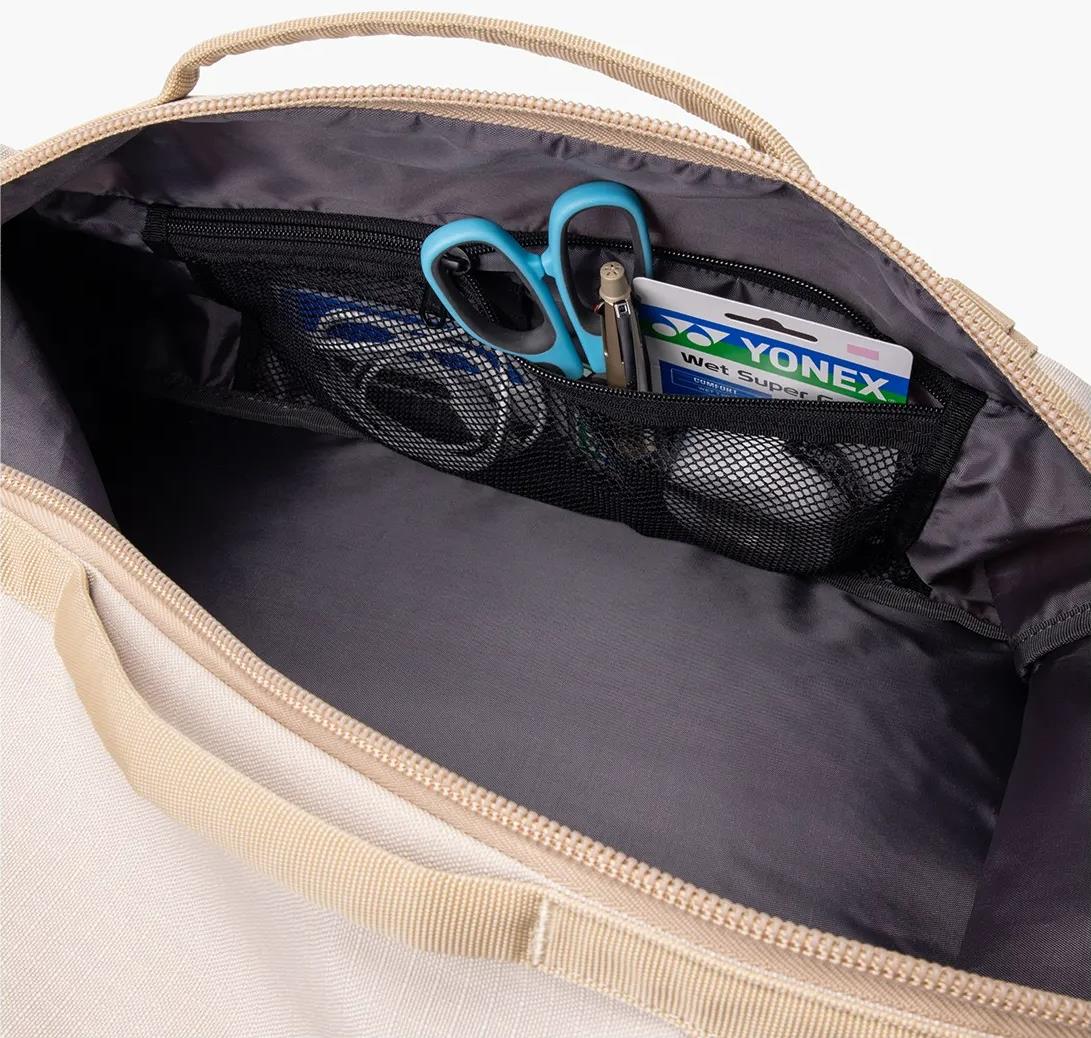 An open Yonex BA72612EX Gearlogic Badminton Backpack in beige shows an inner mesh pocket with blue-handled scissors, a key, and a Yonex wet super grip packet. The main compartment of the Yonex bag is empty.