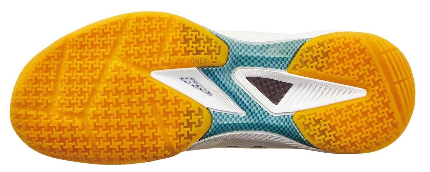 The image shows the sole of Yonex Power Cushion 65Z4 Men's Badminton Shoes in white, with a yellow textured grip, teal midfoot accents, white geometric details, and the Yonex logo at the center—ideal for advanced players.