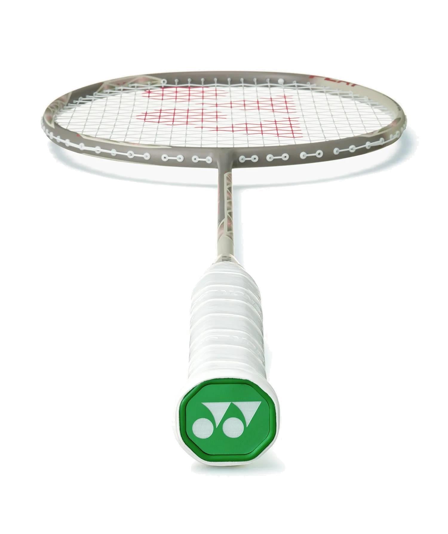 The Yonex Astrox 77 Play 4U Badminton Racket in Light Beige by Yonex is shown lying flat, white grip and green end cap facing the camera, with its graphite frame and strings clearly visible.