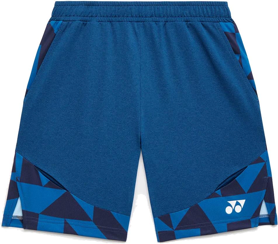The Yonex 15240YX Knit Men's Badminton Shorts in Indigo Blue feature a geometric pattern, elastic waistband, side pockets, quick-dry fabric, and a white Yonex logo on the lower left leg.