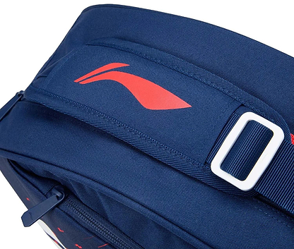 Close-up of the Li-Ning Training Series 3 Racket Badminton Bag in blue/red, featuring a red Li-Ning logo, white buckle on the strap, and a zippered pocket in the lower left for racket accessories.