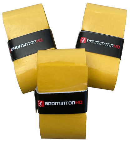 Three BadmintonHQ Sunset Yellow Overgrips from the 3 Pack stand upright, each wrapped with a black band featuring “BADMINTONHQ” in white and red text. Their tacky finish and grouped, angled display highlight the brand’s style.