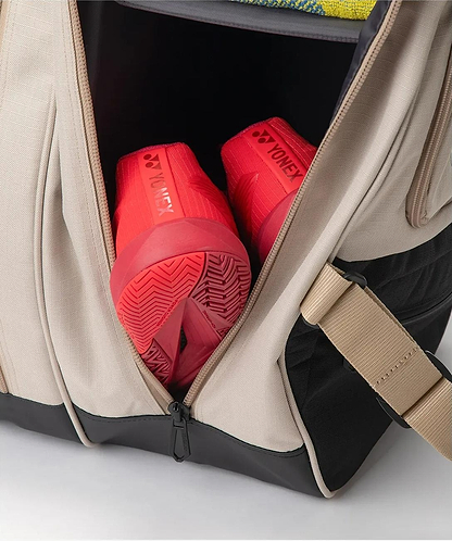 A beige Yonex BA72626EX Gearlogic 6 Racket Badminton Bag, made from recycled polyester, is partially unzipped to display red Yonex athletic shoes organized in a separate compartment.