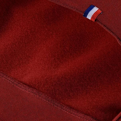 Close-up of the cardinal fabric with a small blue, white, and red striped tag at the seam, showcasing texture and stitching detail. The cotton fleece lends a high-performance look reminiscent of the Tecnifibre Men's Team Badminton Sweater by Tecnifibre.