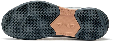 The image shows the sole of Yonex Strider Flow Unisex Badminton Shoes in light grey, displaying a black and beige non-marking textured rubber grip with "YONEX" and "ERGO SHAPE" branding in the center.