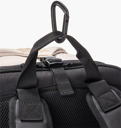 Close-up of the Yonex BA72612EX Gearlogic Badminton Backpack in beige, featuring padded shoulder straps, mesh back padding, a top carrying handle, and a black plastic carabiner attached to an upper loop.