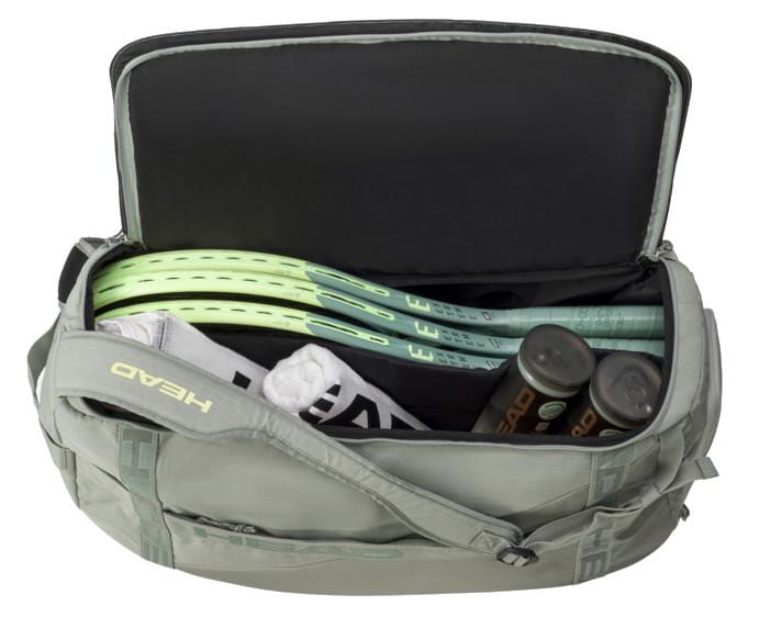 The HEAD Pro Duffle Bag M - LNLL, showcased in gray, can accommodate multiple tennis rackets, a white towel, and two cans of tennis balls. The brand "HEAD" is prominently displayed on the strap and tennis balls—equipment fitting for a professional such as Matteo Berrettini.