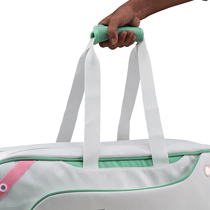 A hand holds the mint green handle of the Li-Ning Competition 6 Racket Badminton Bag in white and green, showing off its stylish upper section with white straps and a pink accent.