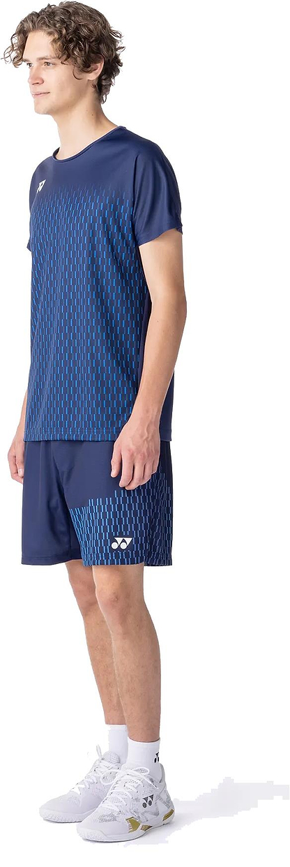 A person wears the Yonex 10713EX Crew Neck Men's Badminton T-Shirt in Dark Navy, featuring a blue geometric pattern, paired with matching navy shorts, white socks, and athletic shoes. The moisture-managing top offers comfort against a white background.