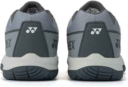 A close-up rear view of light grey Yonex Strider Flow unisex badminton shoes, featuring textured soles, Yonex branding, and a triangular logo on each heel.