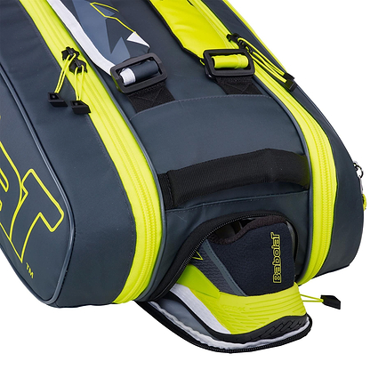 The Babolat RHX6 Pure Aero Racket Bag in grey and yellow showcases a waterproof and durable design. A partially open shoe compartment reveals a Babolat tennis shoe, with the bag's sleek style highlighted by a vibrant yellow zipper and prominent branding from Babolat.