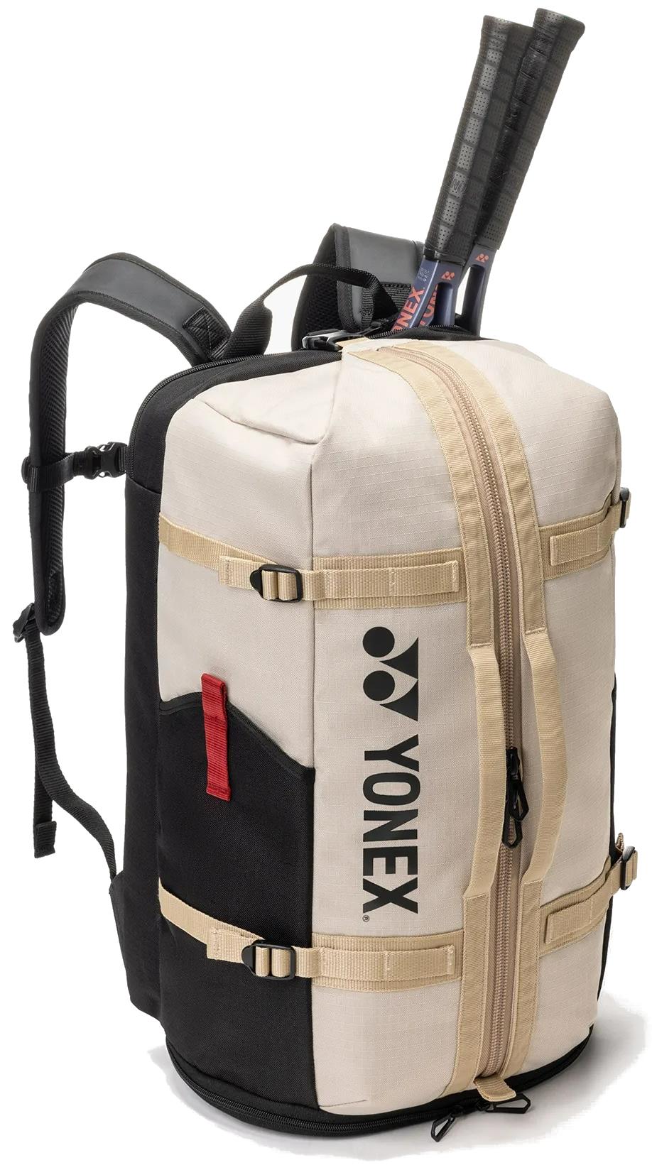 The Yonex BA72612EX Gearlogic Badminton Backpack in beige features tan zippers, side pockets, and shoulder straps. Two racquets protrude from the top compartment, with the Yonex logo visible on the side.