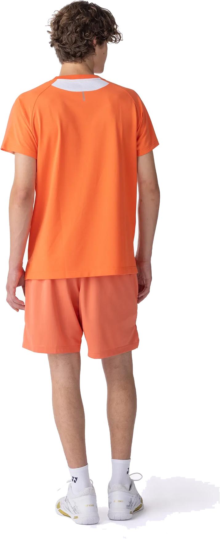 A person with curly hair is seen from behind wearing a Yonex 10711YX Crew Neck Men's Badminton T-Shirt in Cyber Orange, matching shorts, white socks, and white athletic shoes against a plain white background.