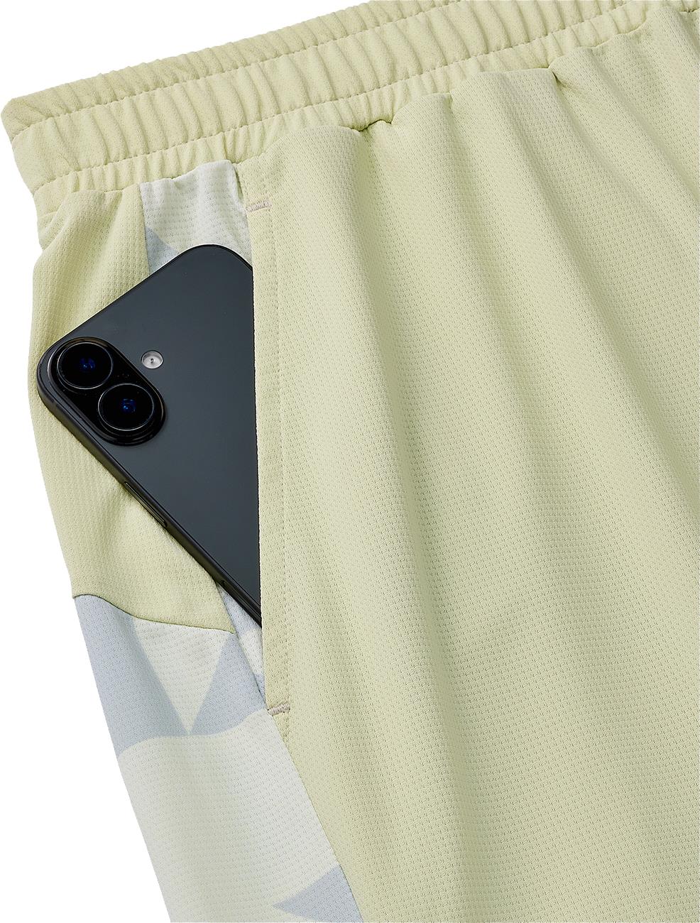 A black smartphone is partially tucked into the side pocket of Yonex 15240YX Knit Mens Badminton Shorts - Champagne, featuring an elastic waistband.