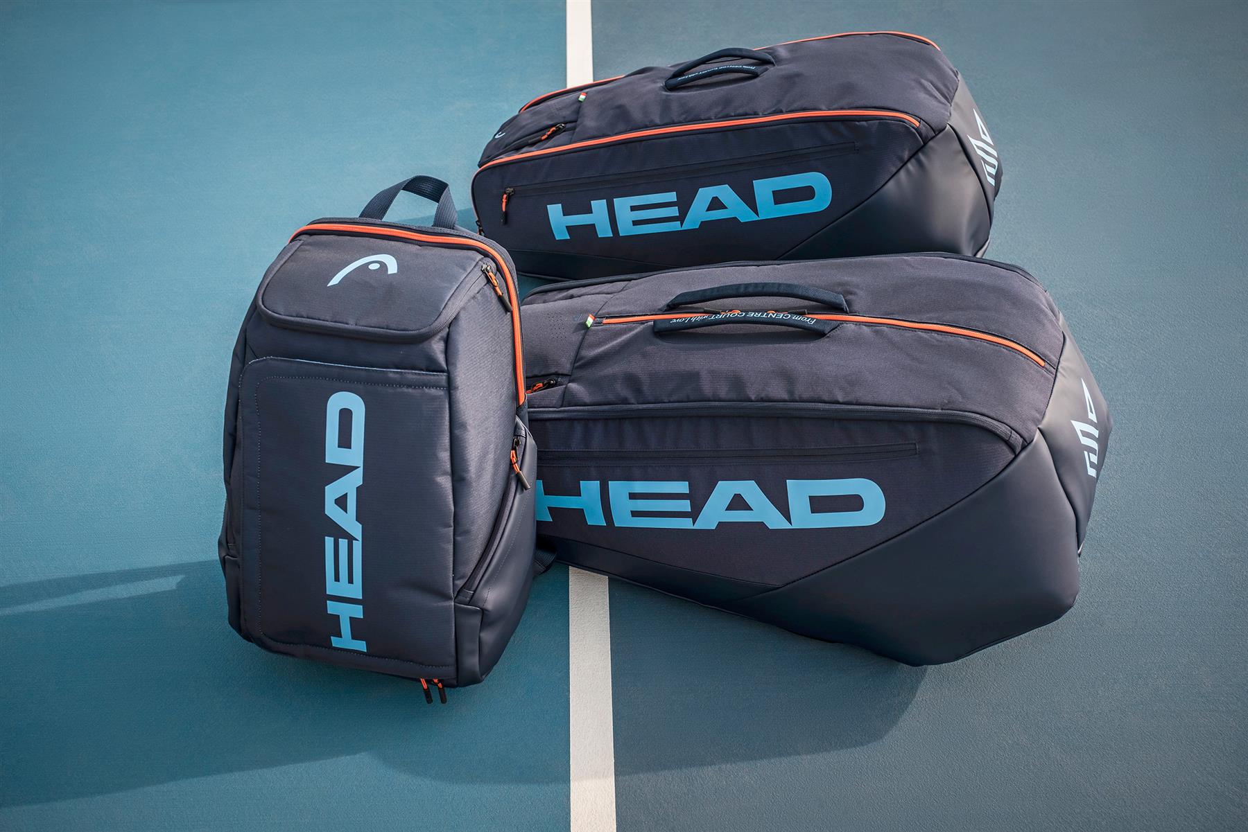 Three HEAD Pro 9 Racket Badminton Bag L - Navy bags, featuring light blue logos, CCT+ climate control, and orange zippers, rest on a blue tennis court near a white line—just like those used by Jannik Sinner.