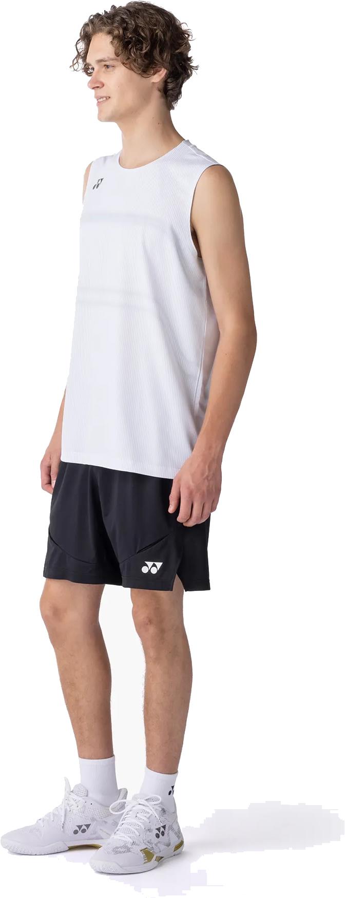 A young man in a white sleeveless athletic shirt, Yonex 15239YX Knit Mens Badminton Shorts - Black, white socks, and white sneakers stands smiling, facing slightly right.