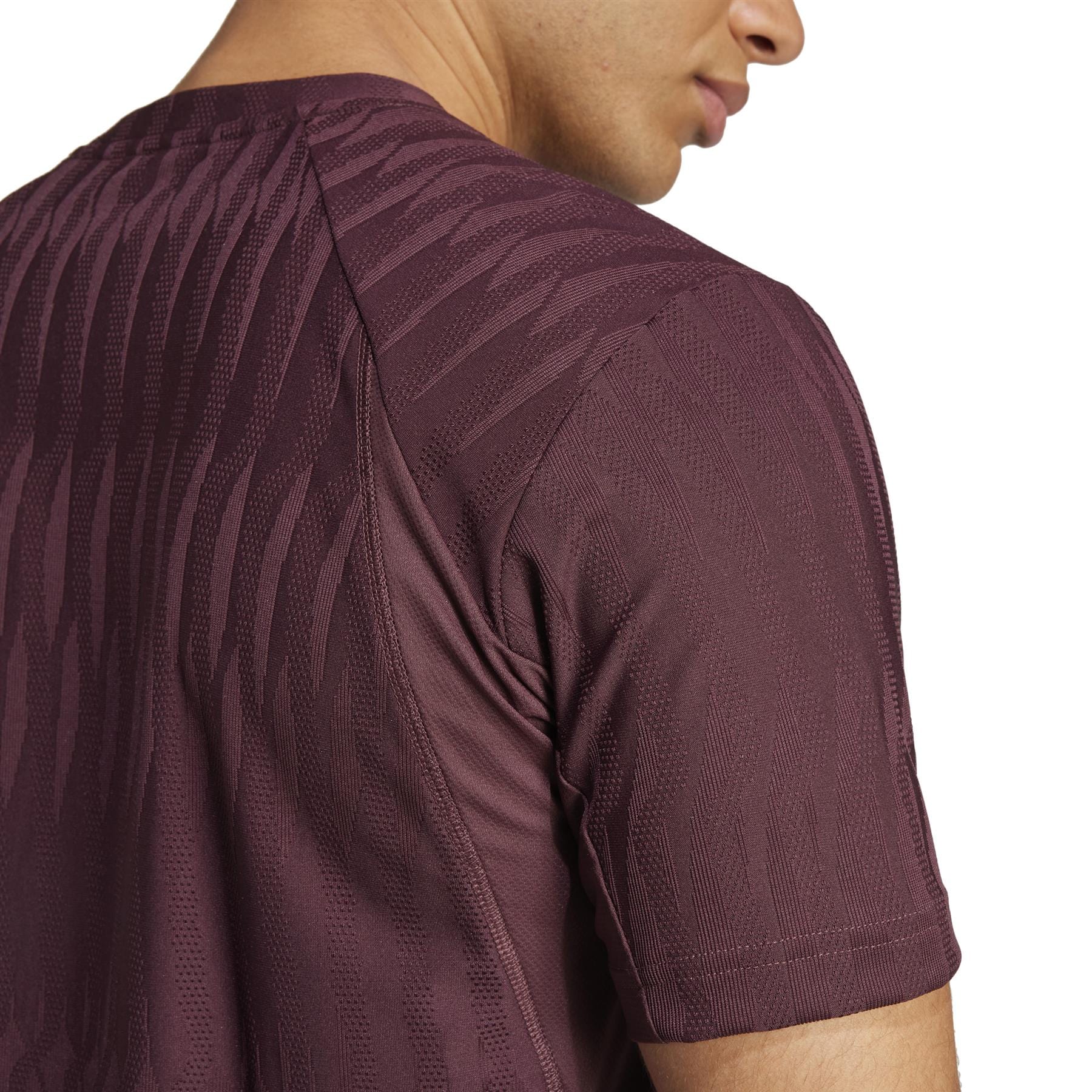 A close-up shows a person in an ADIDAS Men's Climacool+ Freelift Ruby T-shirt with short sleeves, highlighting the subtle diagonal stripe pattern on the upper back and side of the face, emphasizing part of the jawline.