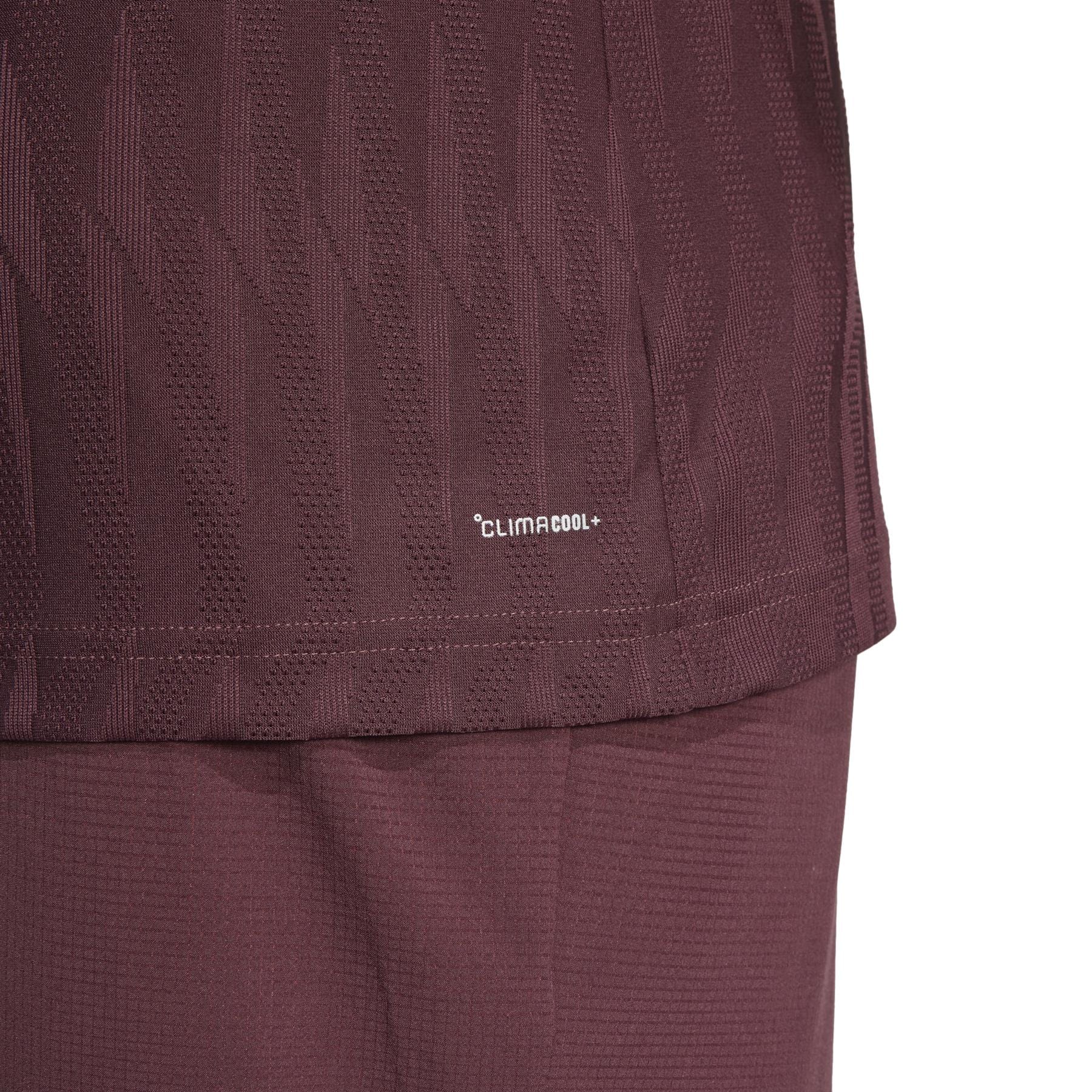 Close-up of the ADIDAS Men's Climacool+ Freelift Badminton T-Shirt in Ruby by adidas, showing a textured geometric design made from recycled materials. The image includes the lower shirt and shorts.