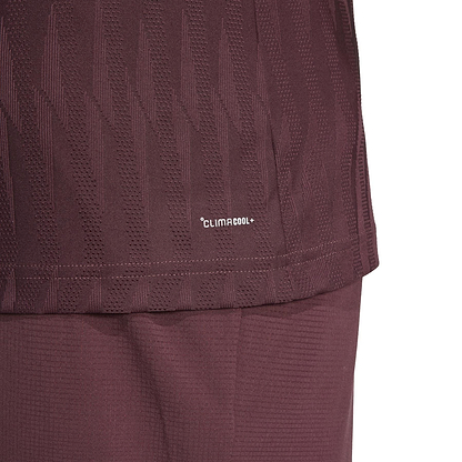 Close-up of the ADIDAS Men's Climacool+ Freelift Badminton T-Shirt in Ruby by adidas, showing a textured geometric design made from recycled materials. The image includes the lower shirt and shorts.