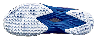 The image displays the sole of a Yonex Power Cushion Aerus Z2 Women's Badminton Shoe in navy blue, featuring a hexagonal tread pattern for grip. Engraved text highlights "Power Cushion," adding to its stylish white and blue design.