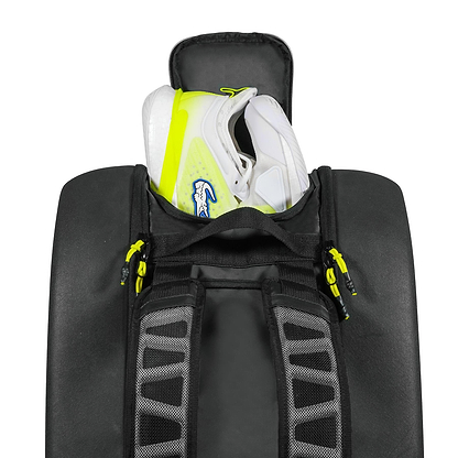 A pair of white sneakers with yellow accents and lightweight EVA soles are partially packed inside a Tecnifibre Reform L Badminton Racket Bag - Black, featuring gray straps and yellow zipper pulls by Tecnifibre.