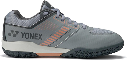 The Yonex Strider Flow Unisex Badminton Shoes in light grey feature orange accents, mesh detailing, laces, and a textured black sole—ideal entry-level footwear for indoor sports or court play.