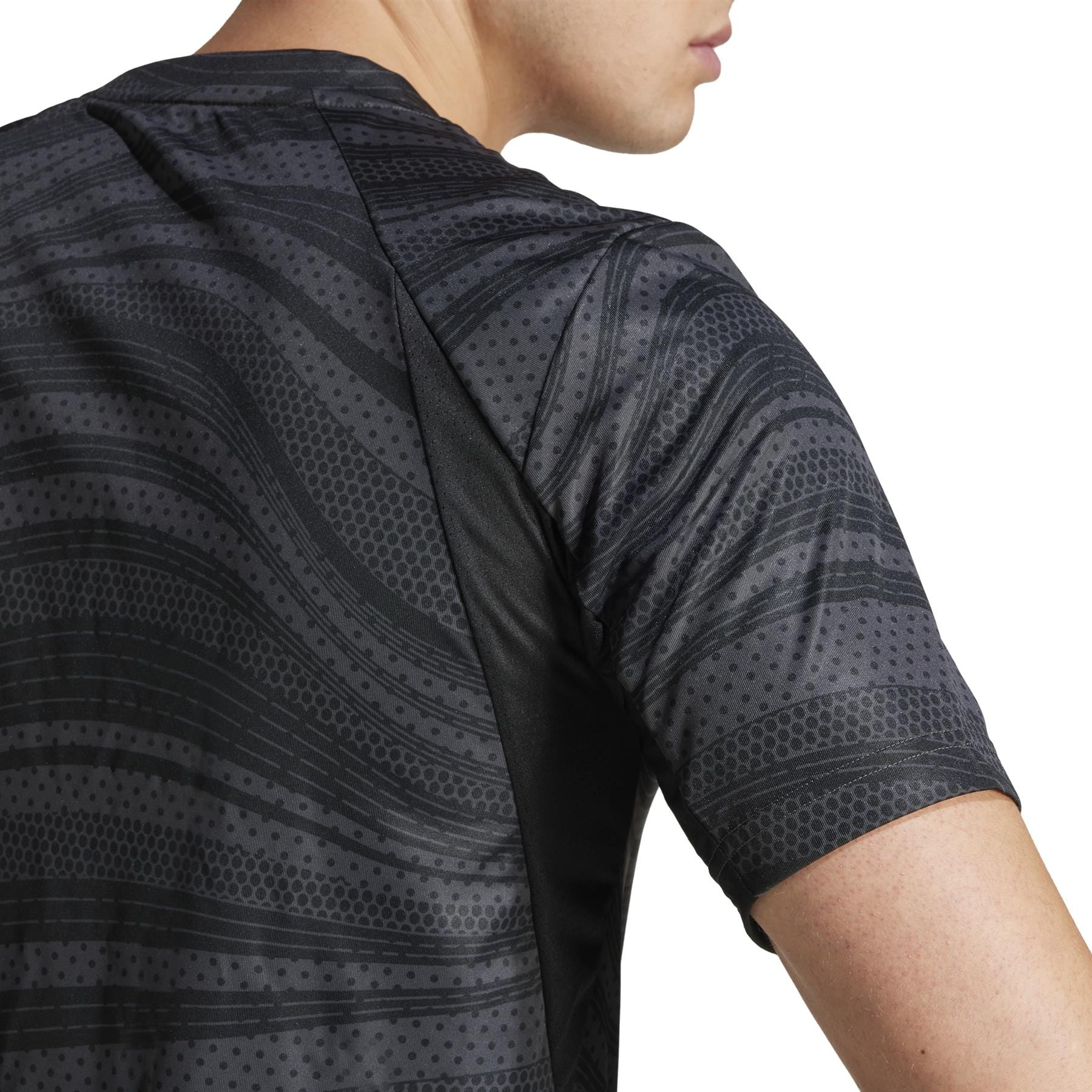 A person is wearing an adidas Club Men's Graphic Badminton T-Shirt in black, made from recycled materials. The shirt has a wavy, dotted design with short sleeves, showcasing style and sustainability from the side view of the upper back and part of the arm.