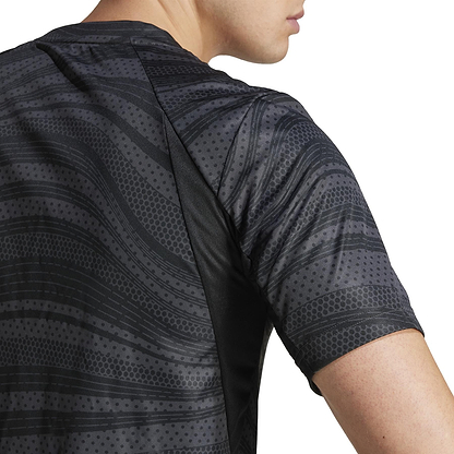 A person is wearing an adidas Club Men's Graphic Badminton T-Shirt in black, made from recycled materials. The shirt has a wavy, dotted design with short sleeves, showcasing style and sustainability from the side view of the upper back and part of the arm.