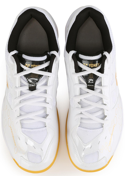 A top view of Yonex Power Cushion SHB 101 Badminton Shoes in white and gold, featuring black inner lining, yellow accents, mesh panels, white laces, light brown-edged soles, and Power Cushion technology for superior shock absorption.
